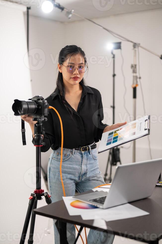 uma legal, atraente ásia fêmea fotógrafo produtor é trabalhando dentro uma tiroteio estúdio. foto