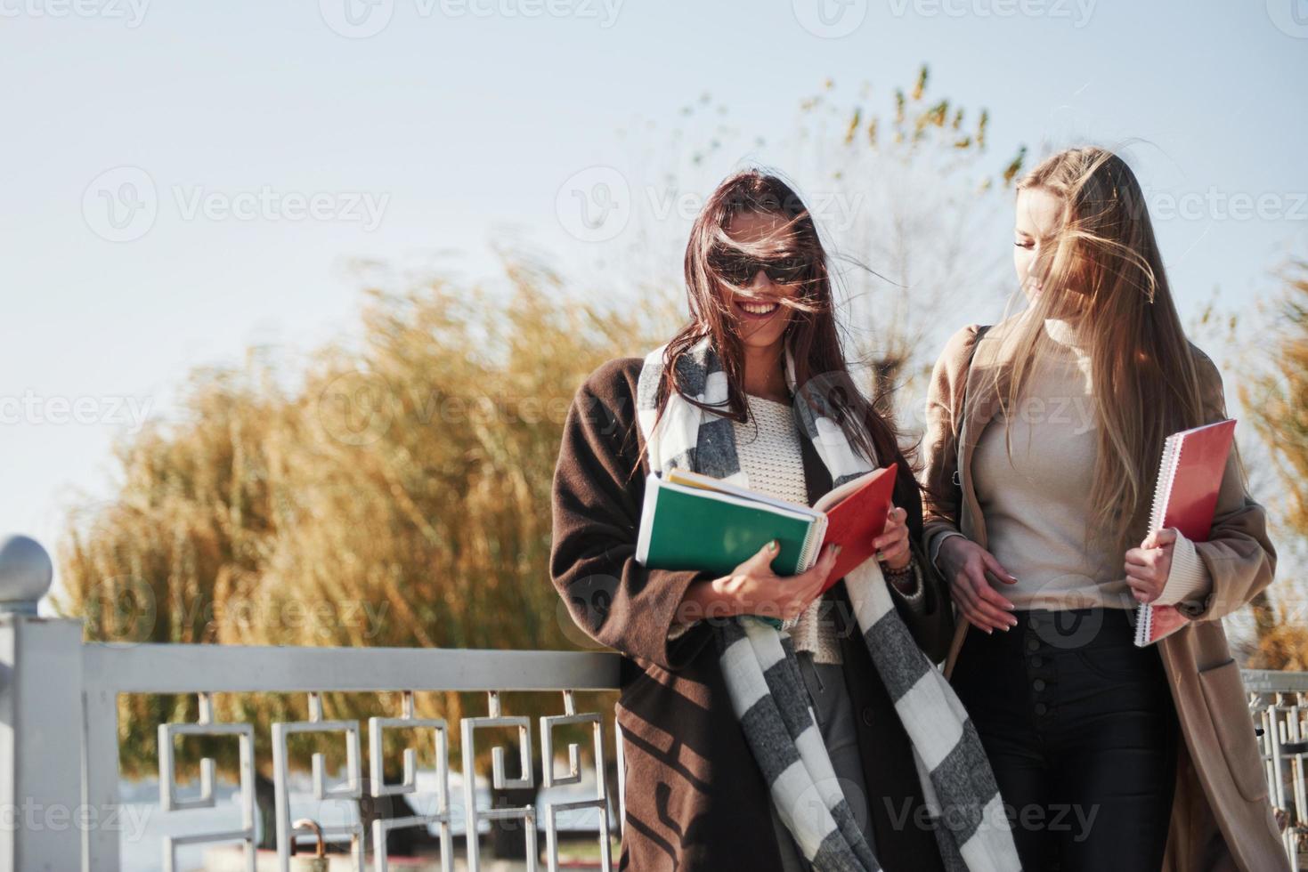 duas estudantes do sexo feminino caminham no parque na ponte segurando blocos de notas foto