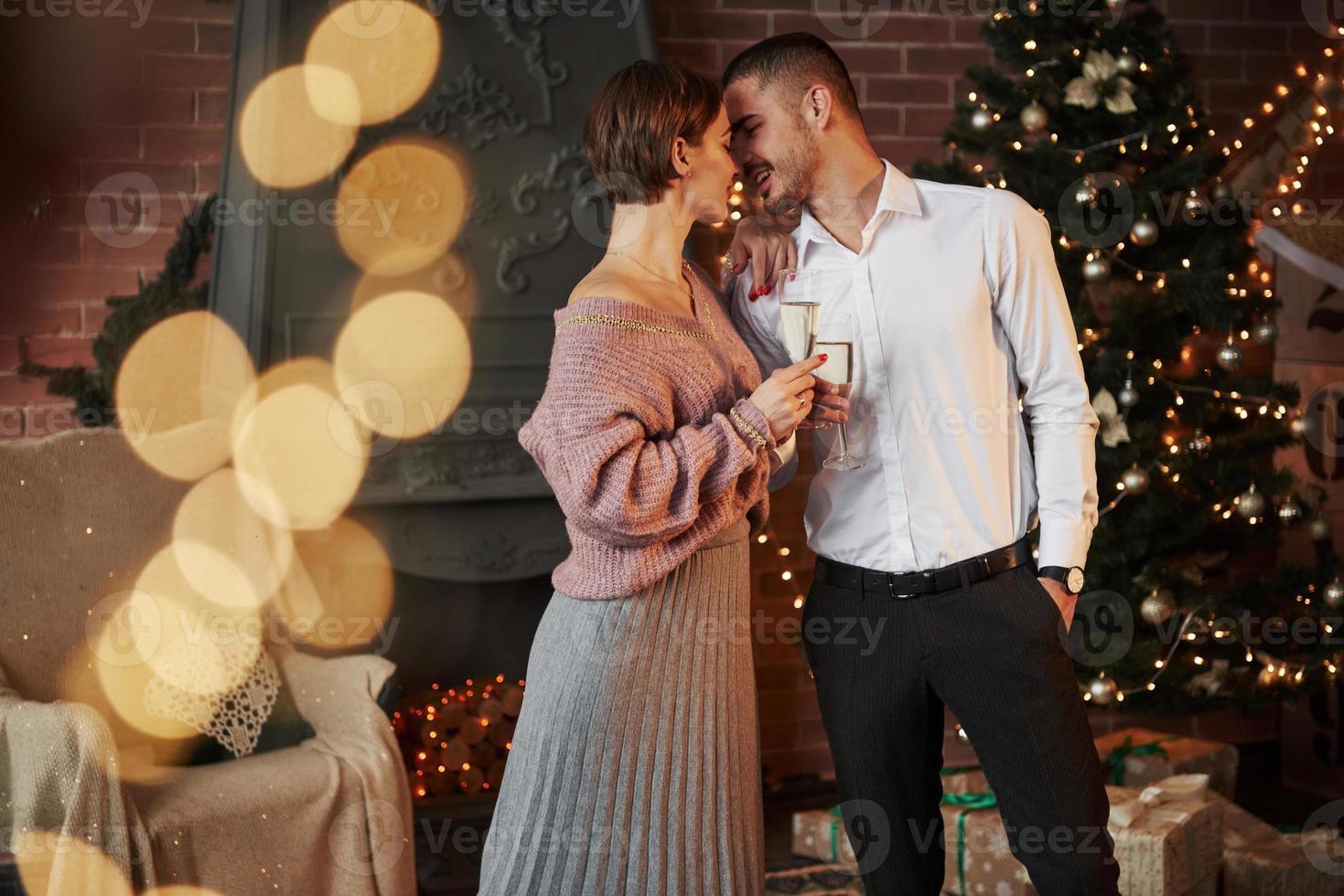 bom passatempo. casal legal comemorando ano novo na frente da árvore de natal foto