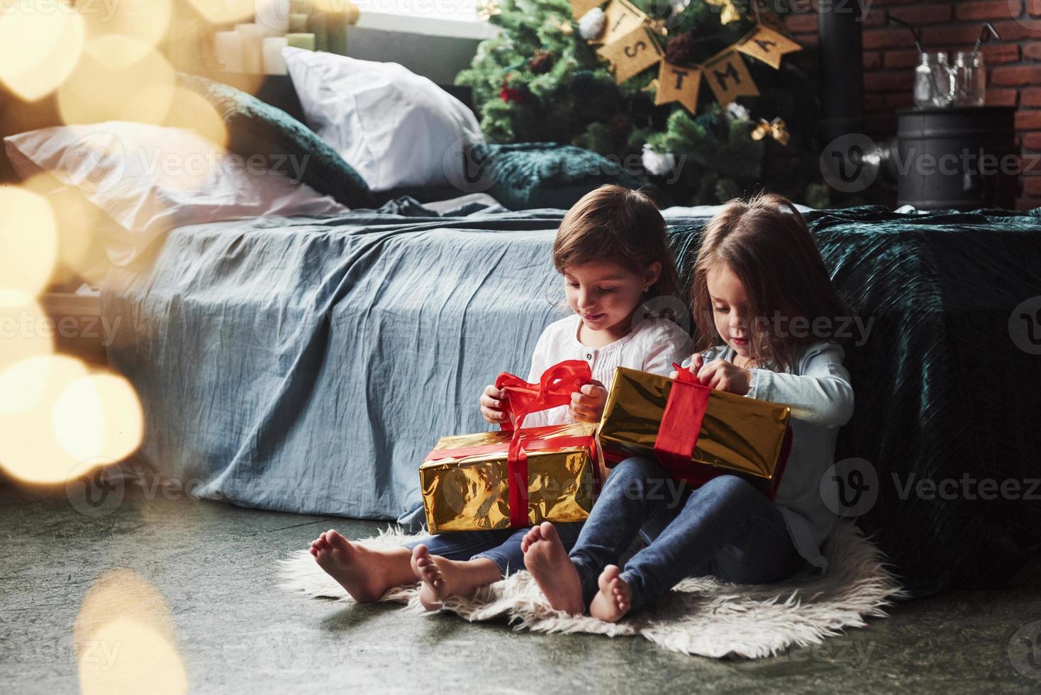 puxe aquelas coisas vermelhas para abrir. férias de natal com presentes para essas duas crianças sentadas dentro de casa no belo quarto perto da cama foto