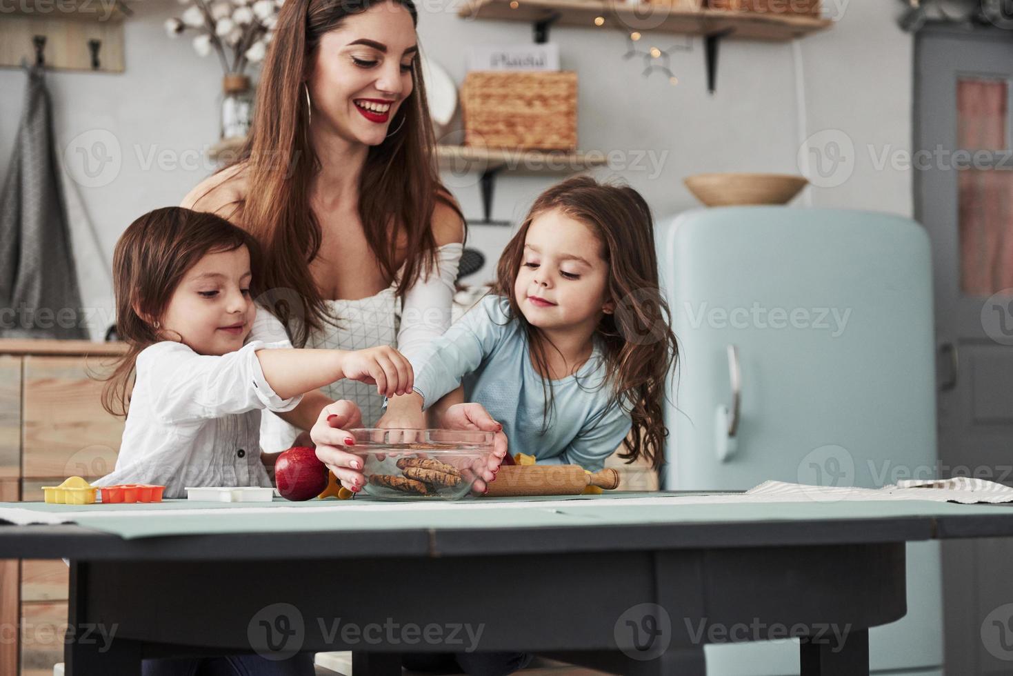 no processo de alcançar essas coisas deliciosas. jovem e linda mulher dando os biscoitos enquanto eles estão sentados perto da mesa com brinquedos foto
