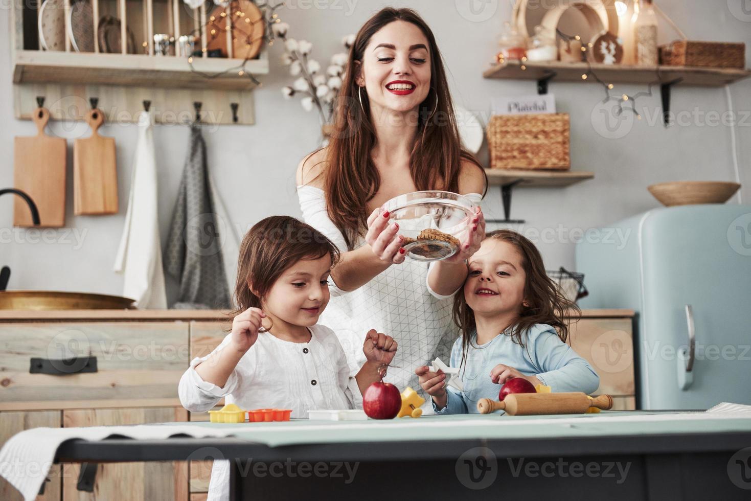 alguns doces não interferem. jovem e linda mulher dando os biscoitos enquanto eles estão sentados perto da mesa com brinquedos foto