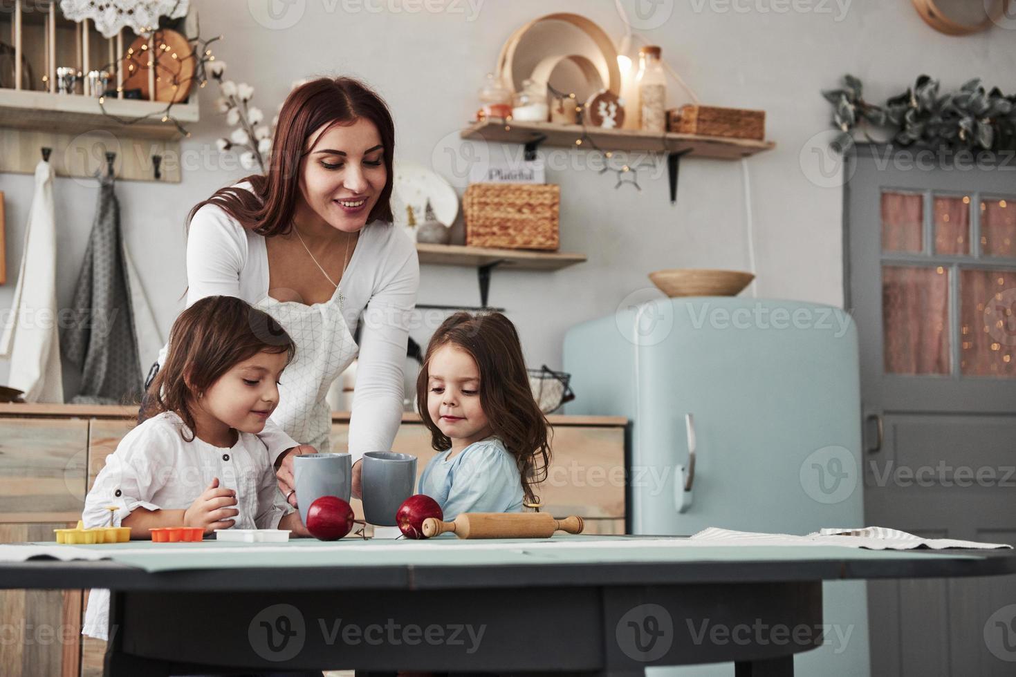 dando algo delicioso. jovem e linda mulher dando bebidas para as crianças enquanto elas estão sentadas perto da mesa com brinquedos foto