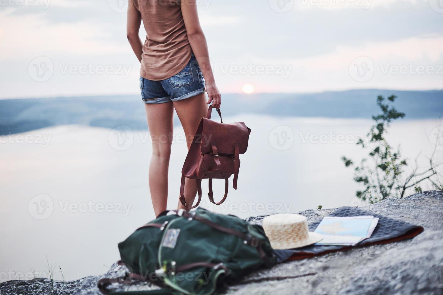 garota solitária em pé perto da borda de uma rocha, observando a bela paisagem, segurando uma bolsa nas mãos foto