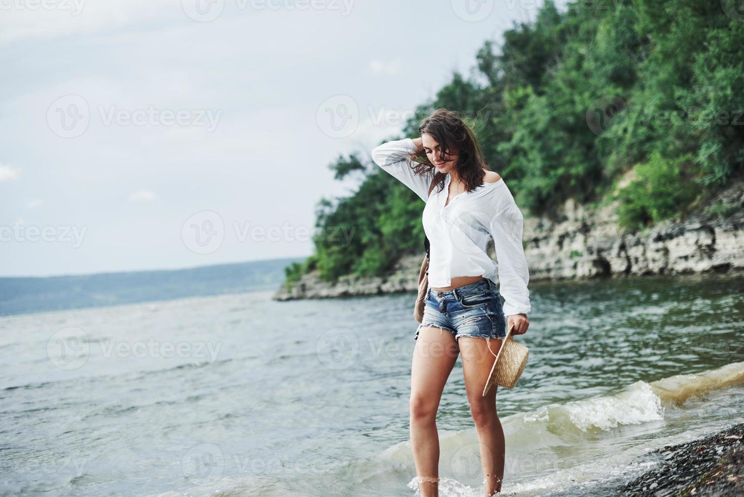 olhar pensativo. linda modelo posando na praia com o fundo do penhasco com árvores foto