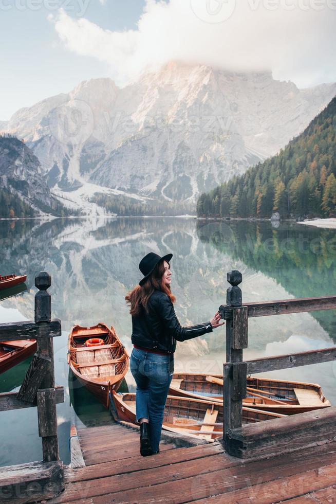 grande distância. nevoeiro no topo das colinas. mulher de chapéu preto apreciando a paisagem montanhosa majestosa perto do lago com barcos foto