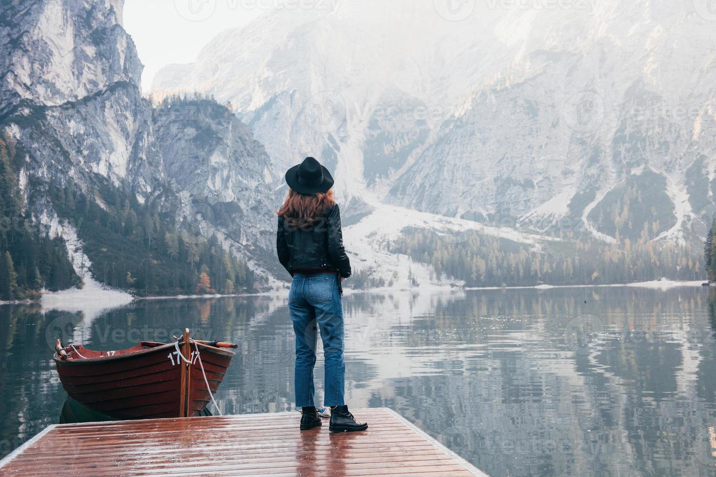 grande aventura. mulher de chapéu preto apreciando a paisagem montanhosa majestosa perto do lago com barco foto