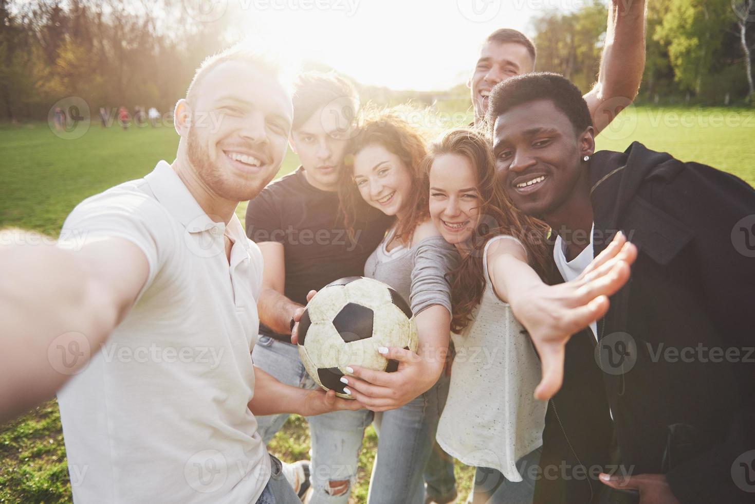 um grupo de amigos em traje casual faz sephi no campo de futebol. as pessoas se divertem e se divertem. descanso ativo e pôr do sol panorâmico foto