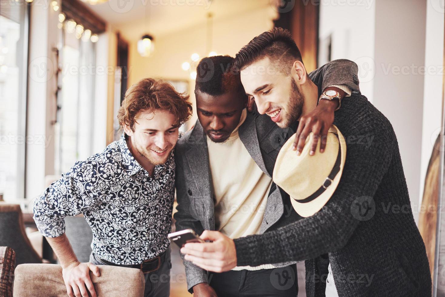 velhos amigos alegres se comunicam uns com os outros e assistem ao telefone no bar. conceito de entretenimento e estilo de vida. pessoas conectadas por wi-fi em reunião de mesa de bar foto