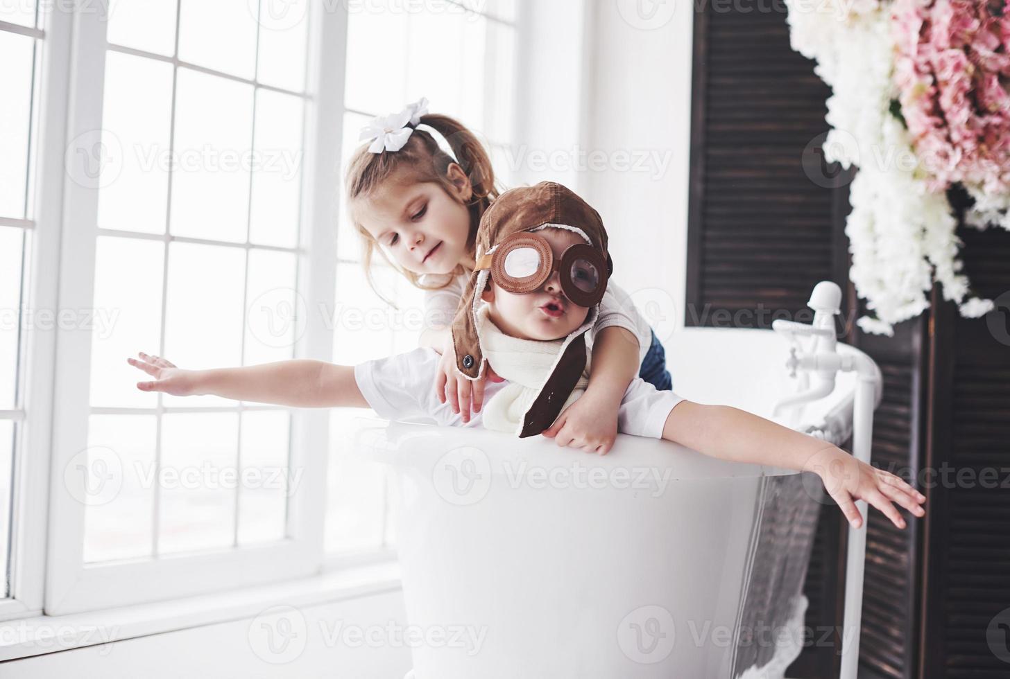 retrato de uma menina e um menino com chapéu de piloto, jogando no banheiro de pilotos ou marinheiros. o conceito de viagem, infância e a realização de sonhos foto