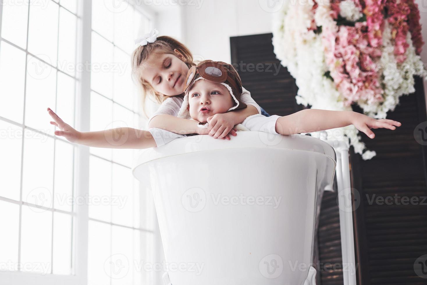 retrato de uma menina e um menino com chapéu de piloto, jogando no banheiro de pilotos ou marinheiros. o conceito de viagem, infância e a realização de sonhos foto