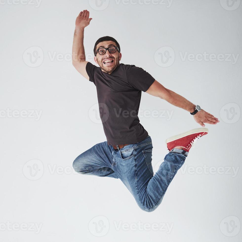 imagem de jovem alegre casual vestido pulando sobre um fundo branco fazendo um gesto diferente foto