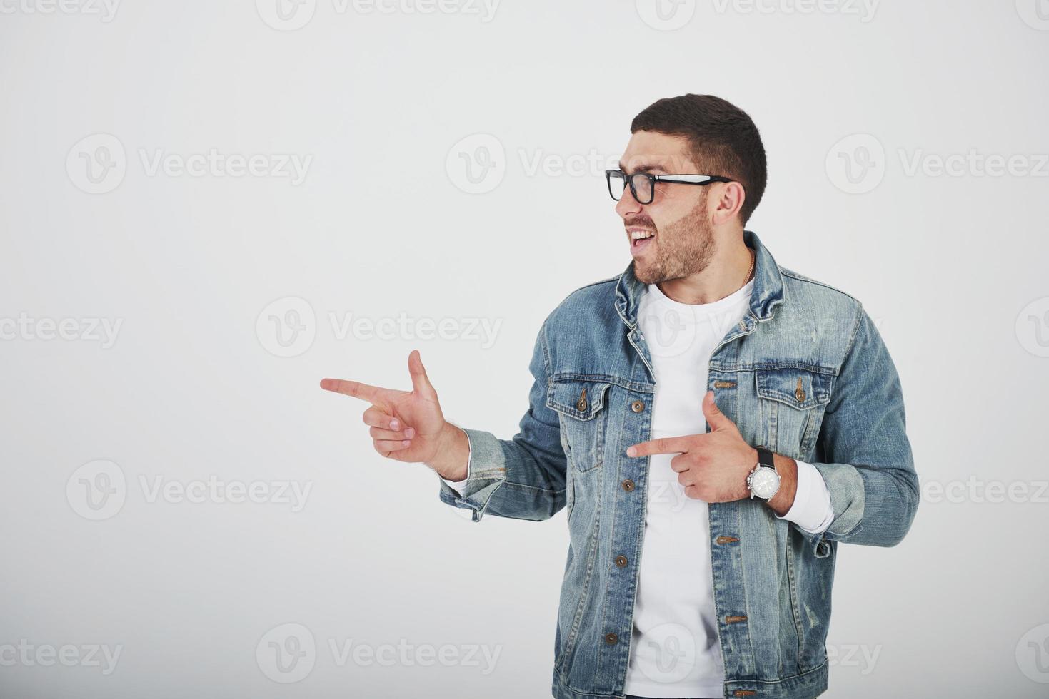 homem barbudo animado feliz usando óculos, olhando para a câmera com um sorriso e apontando para o espaço da cópia com dois dedos isolados sobre um fundo branco foto