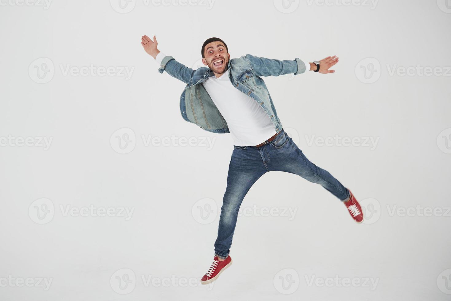 imagem de jovem alegre casual vestido pulando sobre um fundo branco fazendo um gesto diferente foto