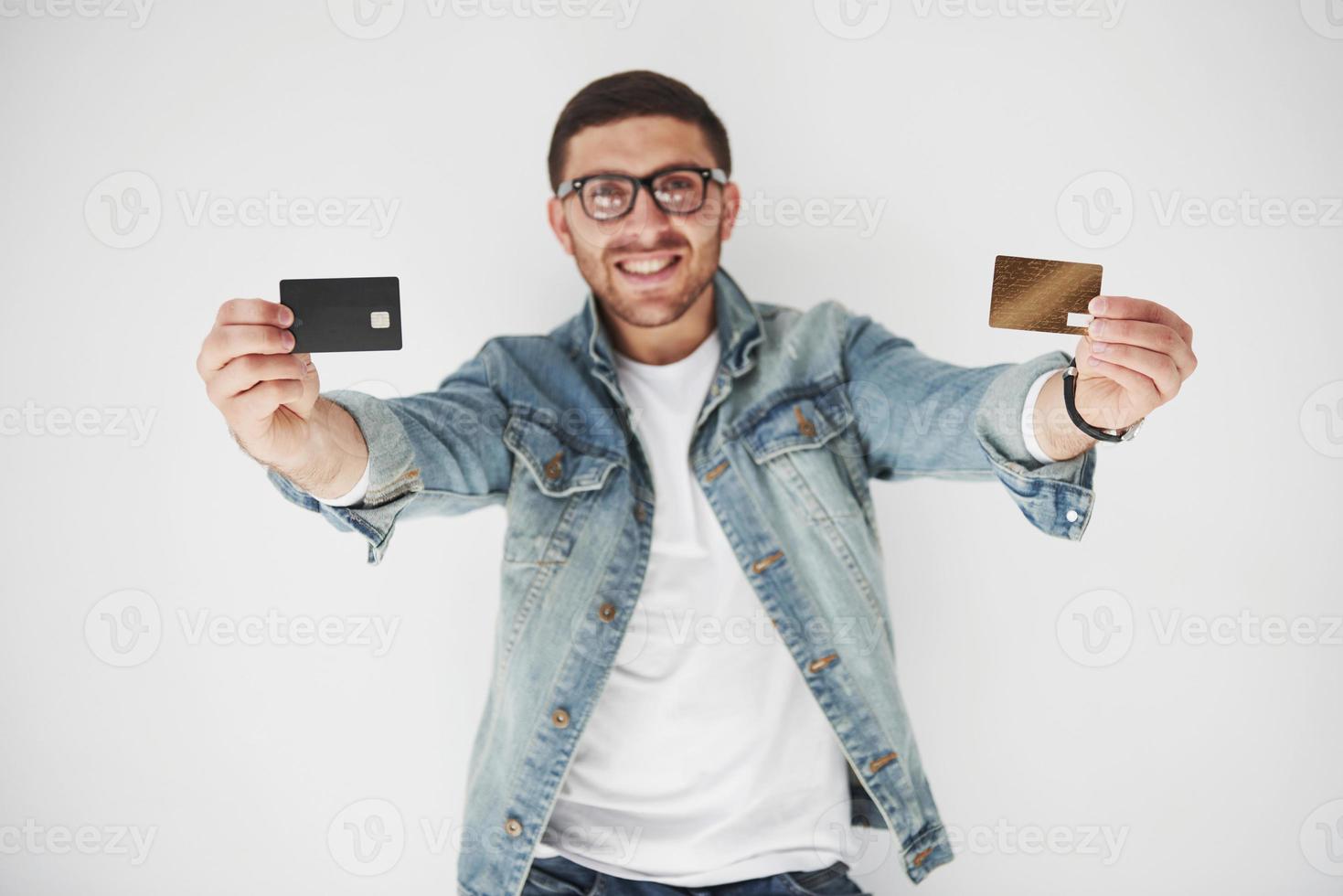 jovem bonito executivo masculino em traje casual, segurando um cartão de crédito nos bolsos em um fundo branco. o conceito de negociação na internet e a facilidade do dinheiro eletrônico foto