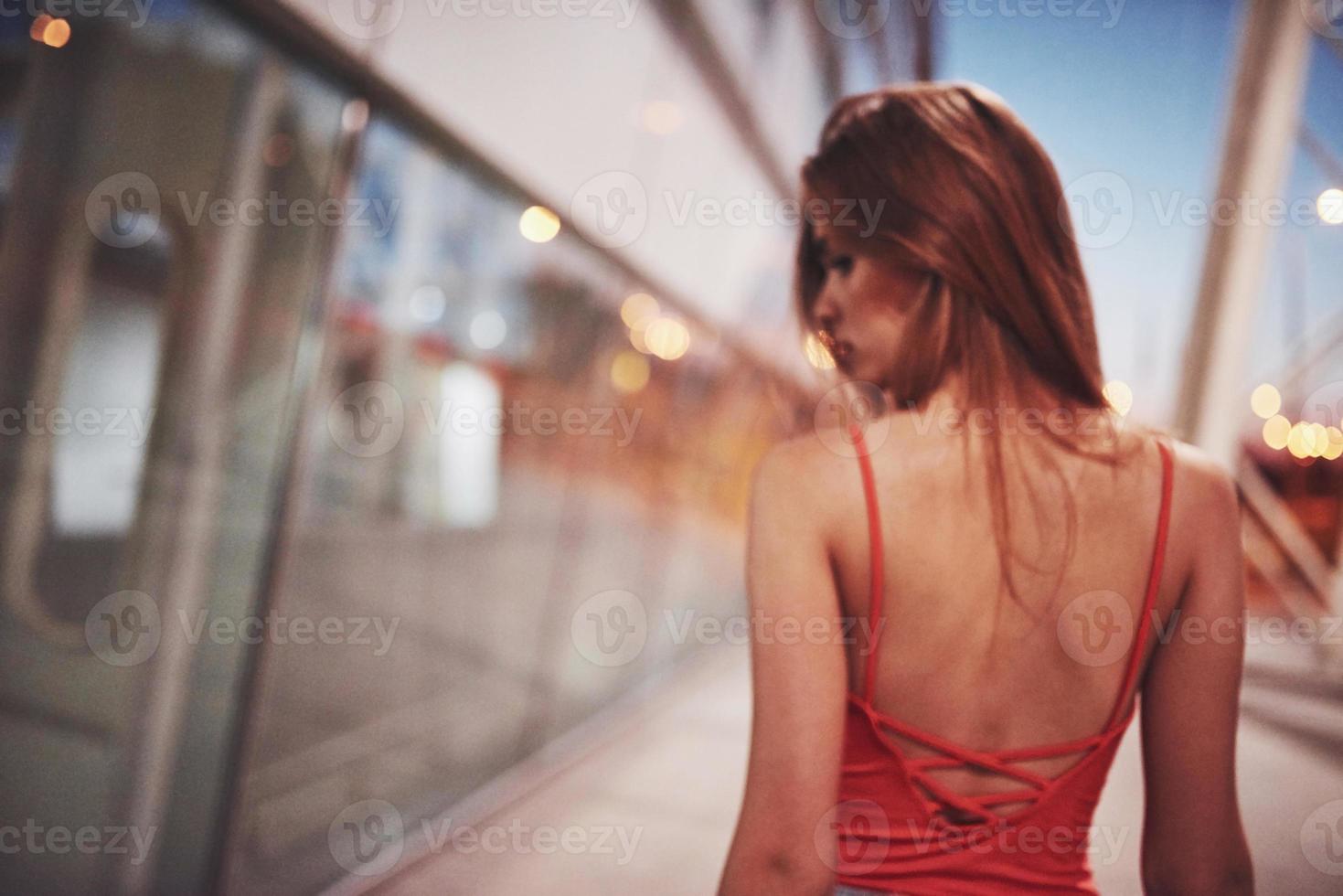 garota linda turista sexy andando na rua movimentada da cidade, perto do aeroporto. mulher olhando para a câmera ao ar livre com uma camiseta vermelha da moda foto