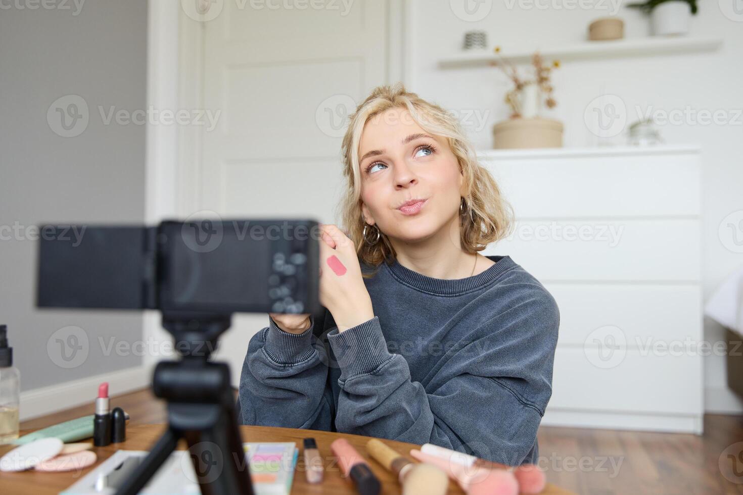 retrato do jovem criativo social meios de comunicação conteúdo O Criador, mulher mostrando batom amostras em dela mão, gravação sobre beleza e inventar, sentado dentro dela quarto dentro frente do digital Câmera foto