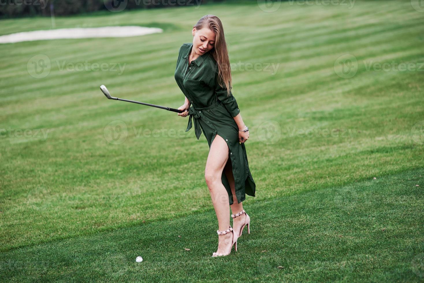 linda mulher vestida de verde em pé no campo de golfe com um taco na mão, posando para a foto