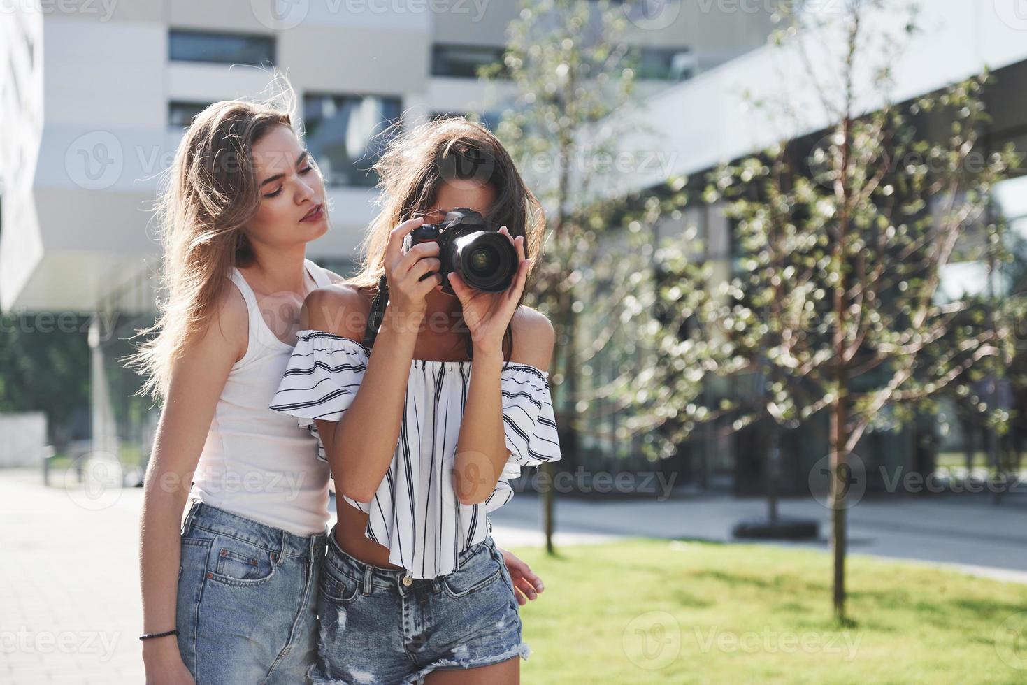 duas amigas lindas da menina com a câmera tiram fotos juntas e caminham pela cidade