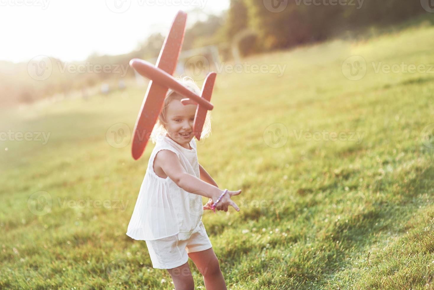 lançar no ar. menina feliz correndo no campo com um avião de brinquedo vermelho nas mãos foto