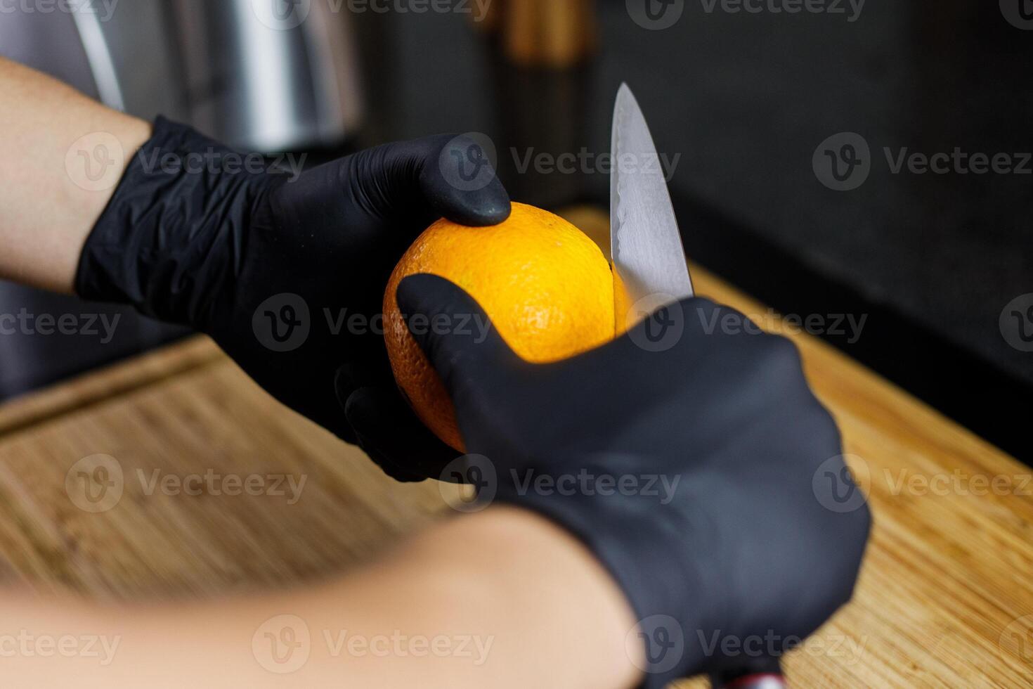 homem corte laranja descasca com Preto luvas japonês faca em de madeira corte borda foto