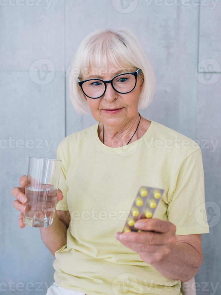 mulher sênior em copos segurando um remédio e um copo de água. idade, cuidados de saúde, conceito de tratamento foto