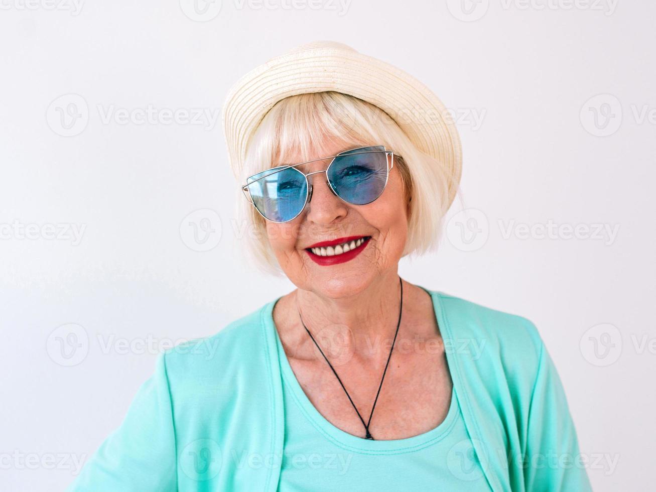 mulher alegre elegante sênior em óculos de sol azuis e roupas turquesas. verão, viagem, anti-idade, alegria, aposentadoria, conceito de liberdade foto