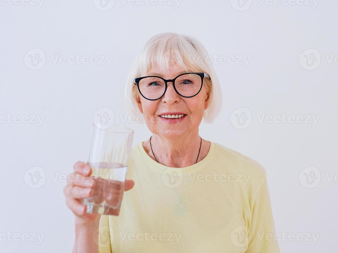 sênior mulher segurando um copo de água e água potável. estilo de vida saudável, esporte, conceito anti-idade foto