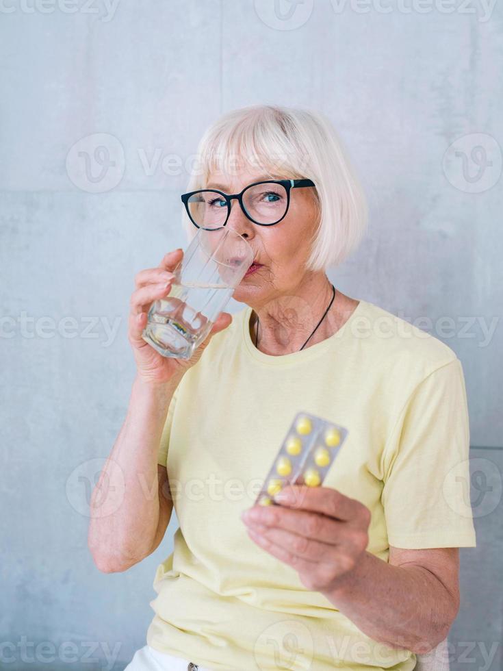 mulher sênior em copos segurando um remédio e um copo de água. idade, cuidados de saúde, conceito de tratamento foto