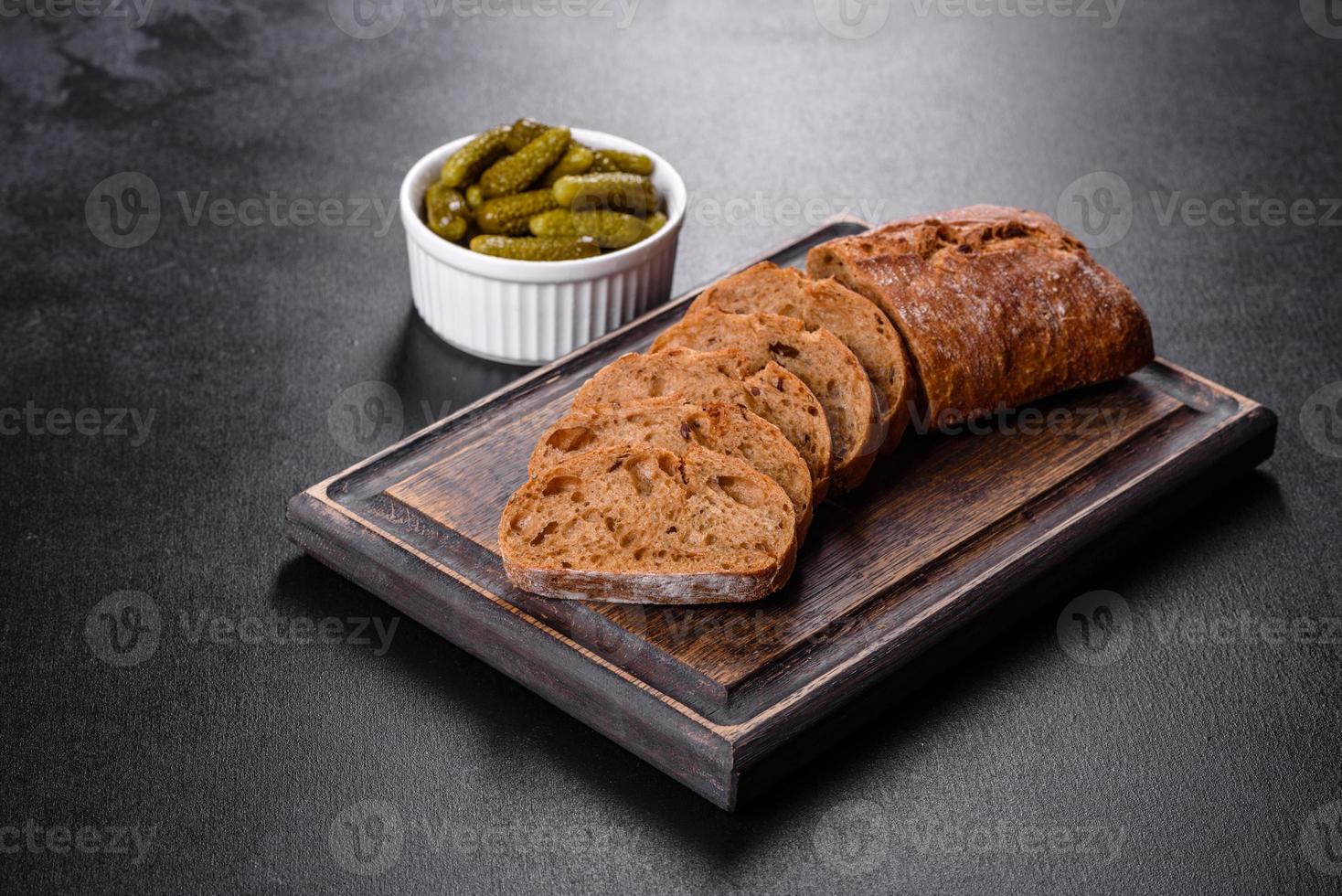 delicioso pão preto fresco fatiado com fatias em um fundo escuro de concreto foto