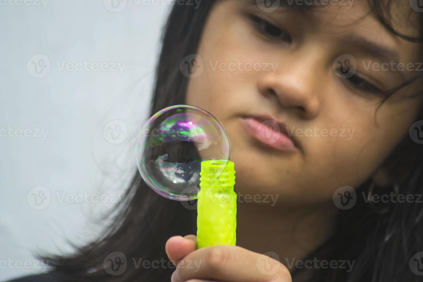 uma garota segurando um fabricante de bolhas e soprando-os para fora. foto