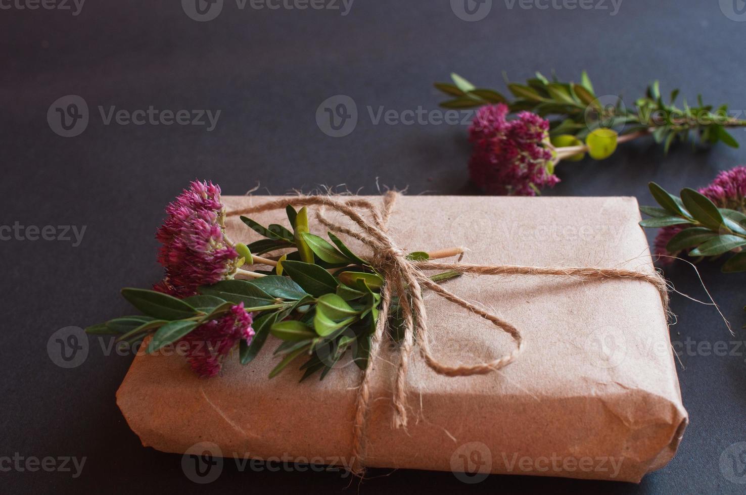 caixa de presente artesanal com nó natural com florzinhas rosa em fundo preto. foto