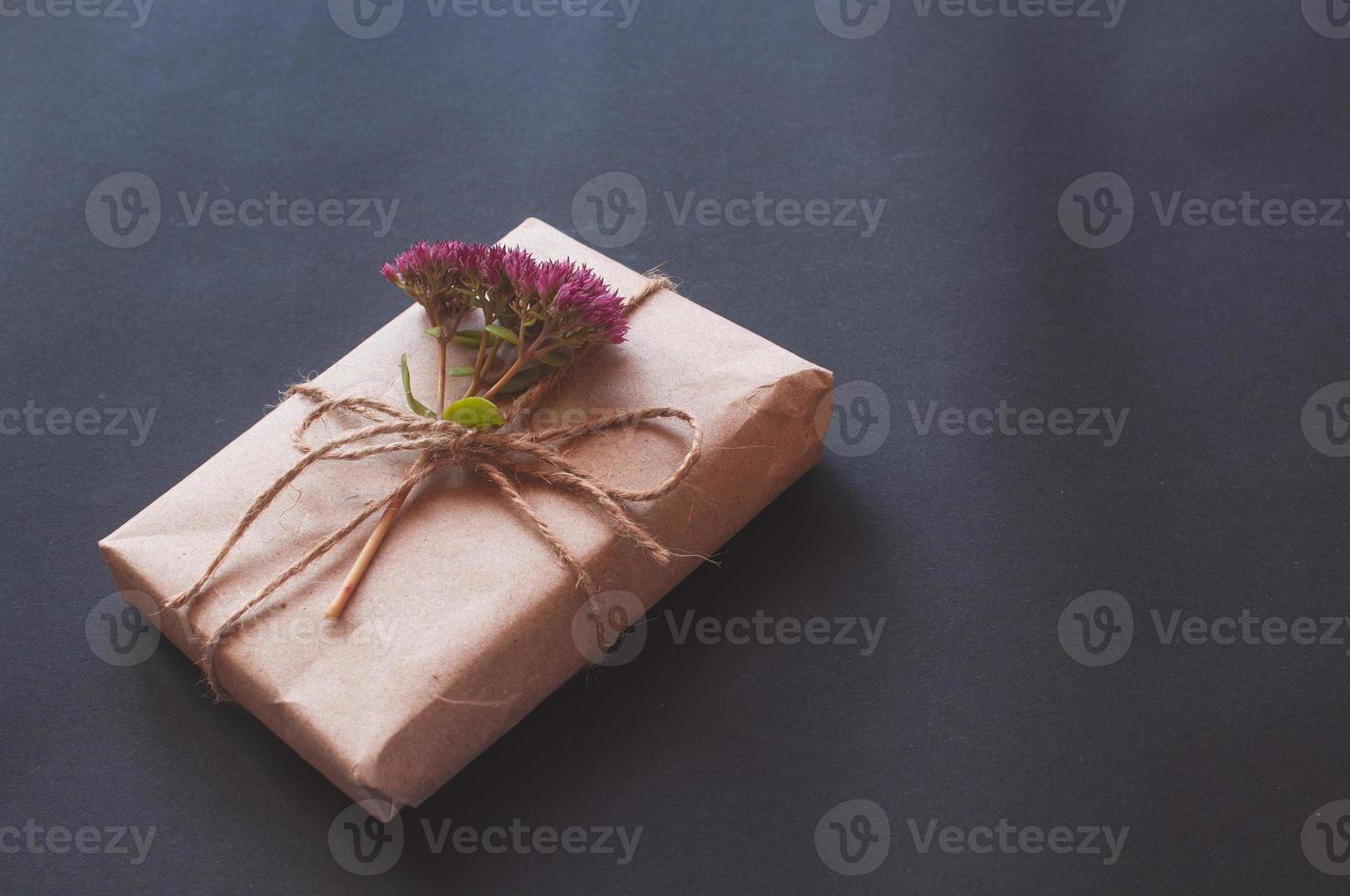 caixa de presente artesanal com nó natural com florzinhas rosa em fundo preto. foto