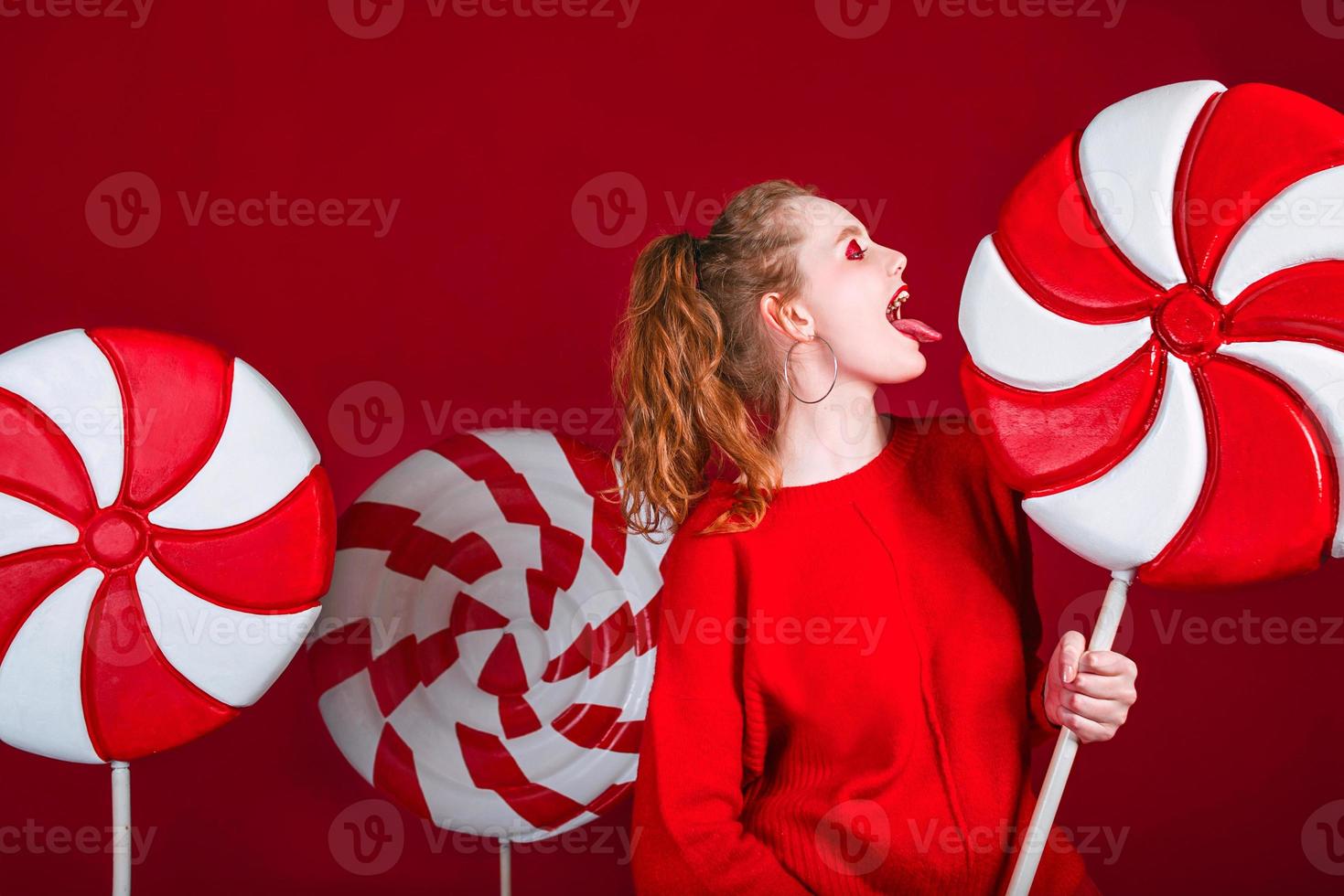 retrato de mulher bonita ruiva engraçada de natal surpreendeu doces no fundo vermelho foto