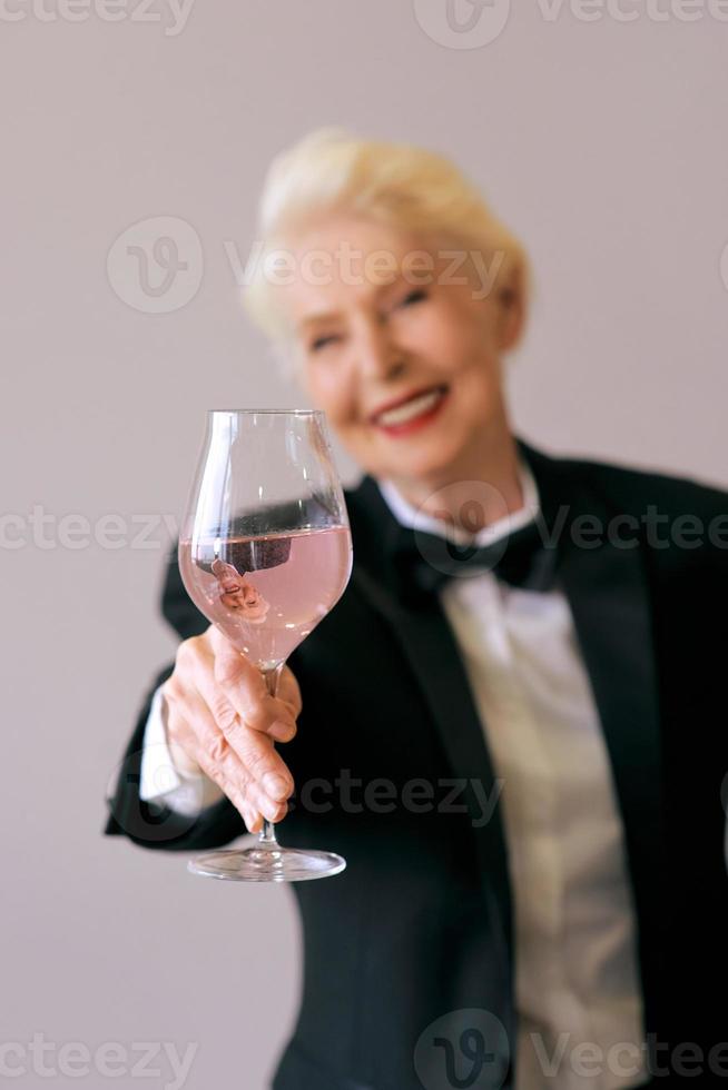 elegante sommelier maduro mulher sênior de smoking com copo de vinho. diversão, festa, estilo, estilo de vida, trabalho, álcool, conceito de celebração foto