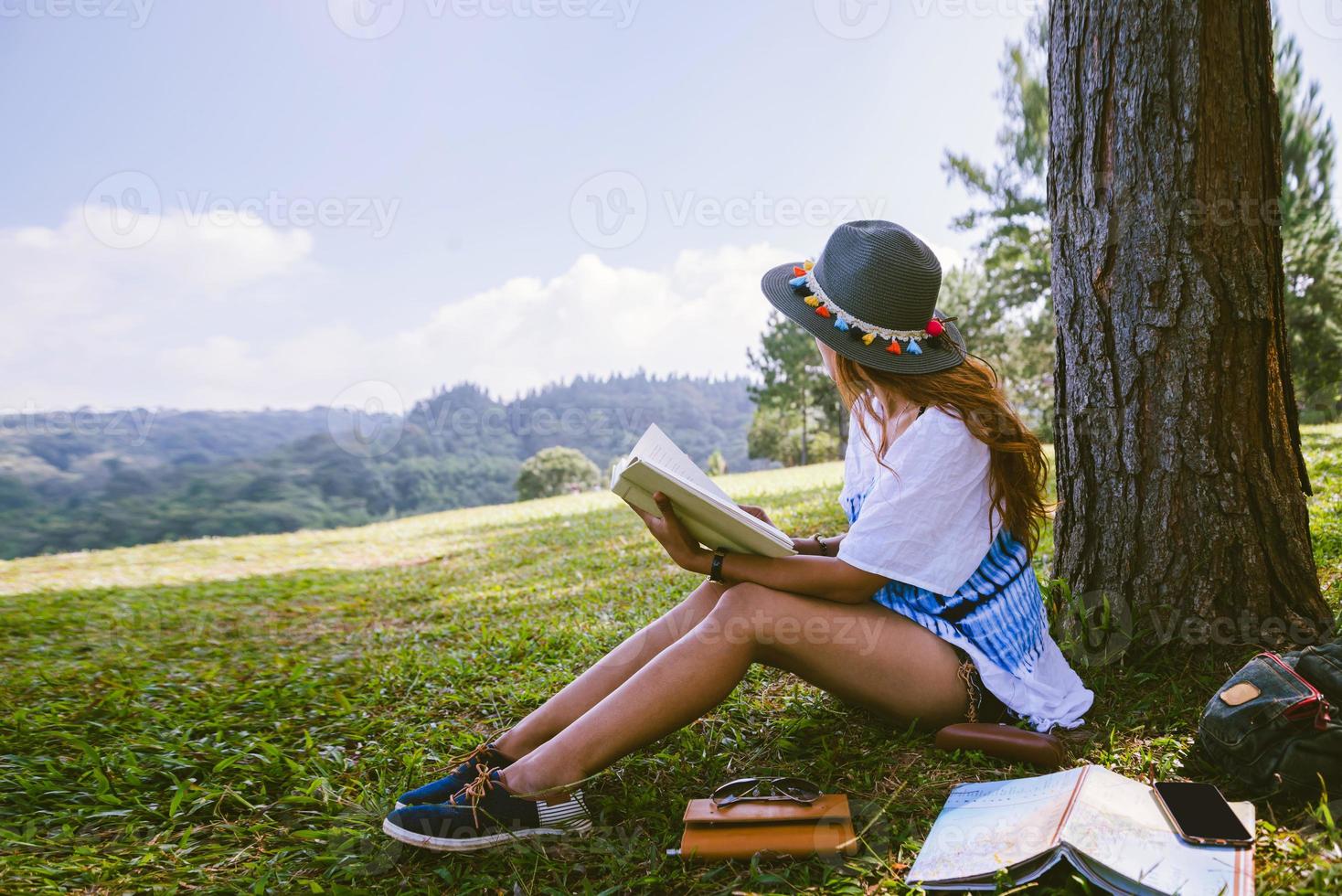 mulher asiática viajar natureza. viajar relaxar. menina sentada lendo um livro debaixo da árvore. linda garota na floresta de outono, lendo um livro de educação da natureza e escrever uma nota. foto