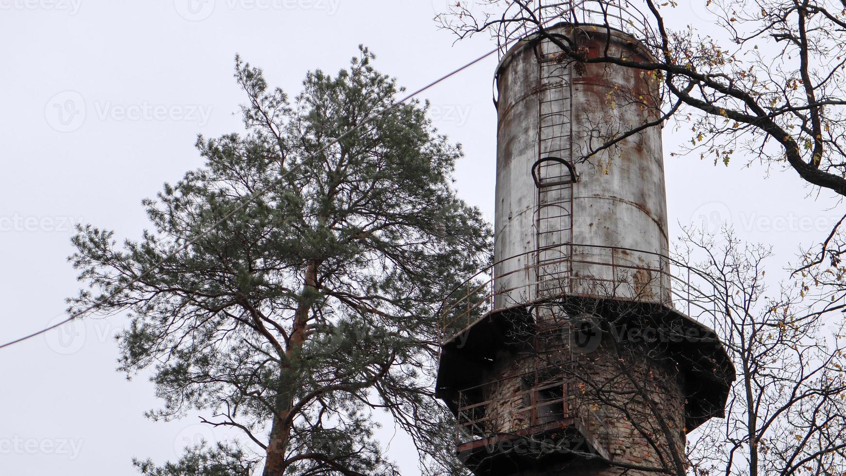 o tubo da planta se eleva acima da floresta. paisagem industrial. produção ecológica sem fumaça de cachimbo. torre de água na aldeia. abastecimento de água às casas sob pressão. paisagem rural. foto