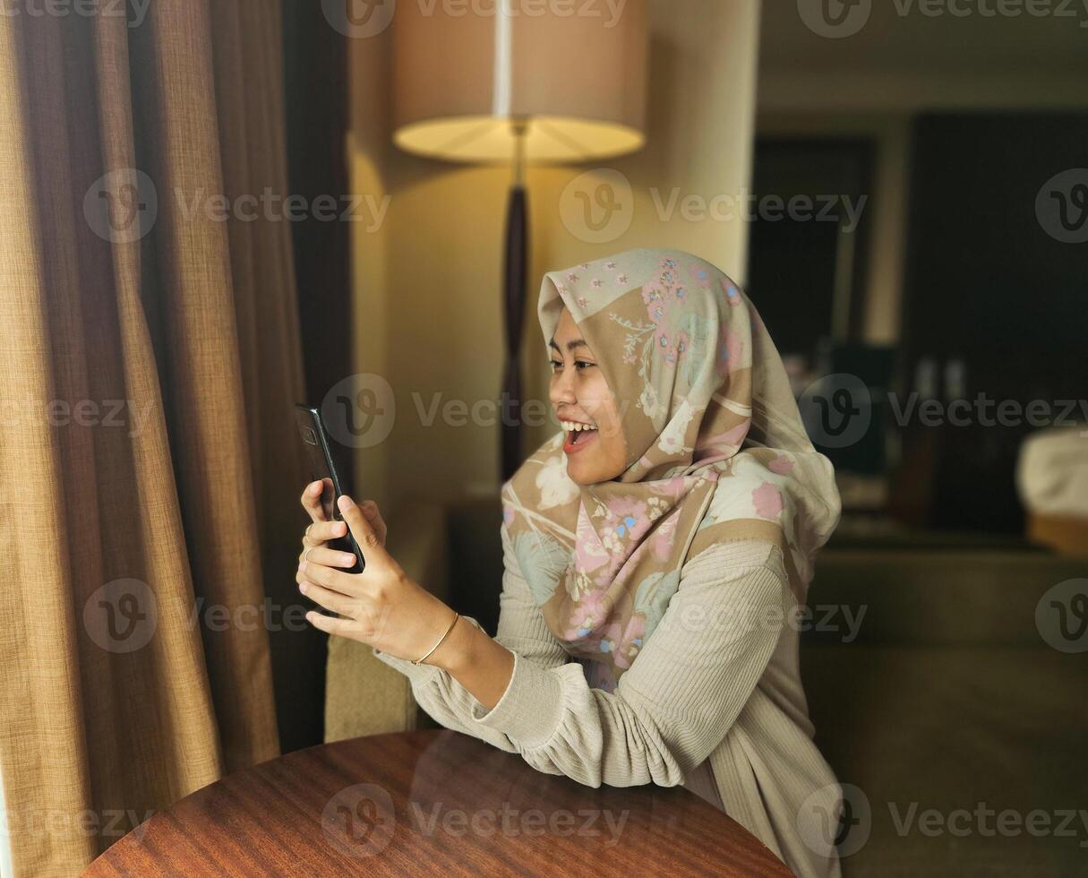 feliz ásia muçulmano mulher vestindo hijab sorridente quando lendo texto mensagem ou bate-papo em dela telefone com borrão fundo, comunicação em telefone, moderno global Internet social meios de comunicação conceito foto