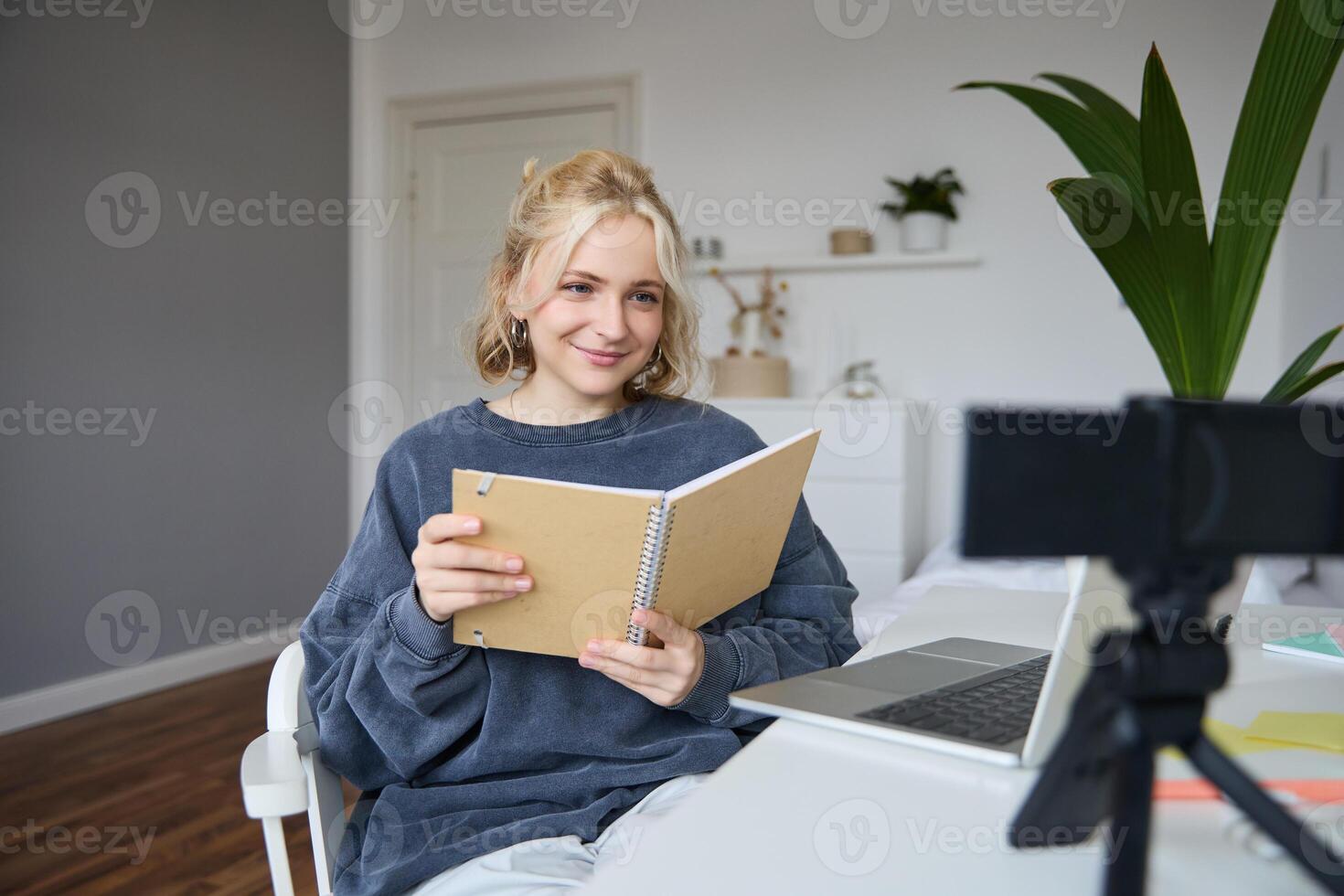 jovem sorridente loiro mulher, senta perto computador portátil, usa digital Câmera para registro blog, cria estilo de vida conteúdo para social meios de comunicação, registros tutorial, mostra caderno, lê dela notas foto