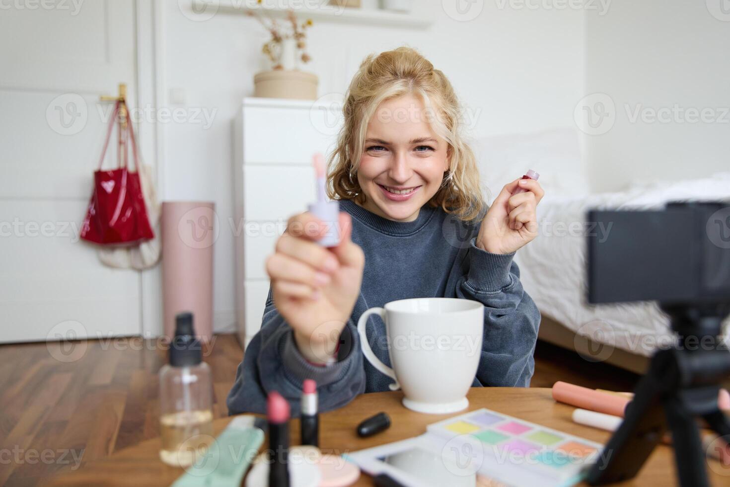 estilo de vida, beleza blogueiro, mulher gravação do dela colocando em inventar, falando para Câmera, fazer conectados tutorial, mostrando dela lábio lustro ou batom para seguidores, sentado em chão com copo do chá foto