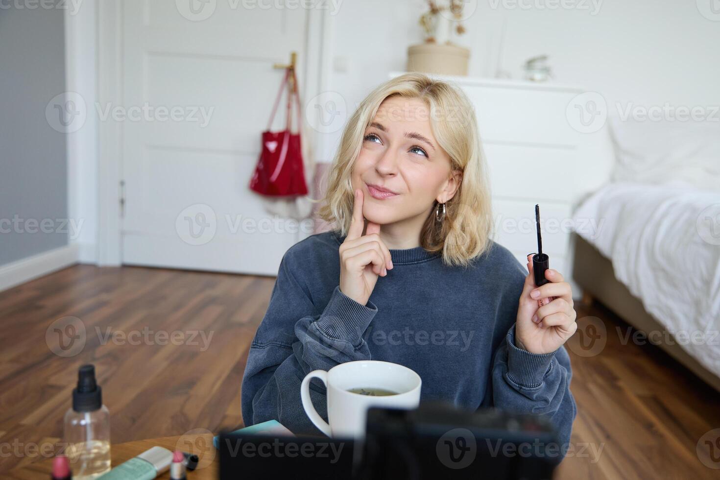 retrato do jovem carismático mulher, menina registros enquanto colocando em inventar, revendo beleza produtos para social meios de comunicação conta, tem uma estilo de vida blog, segurando rímel foto