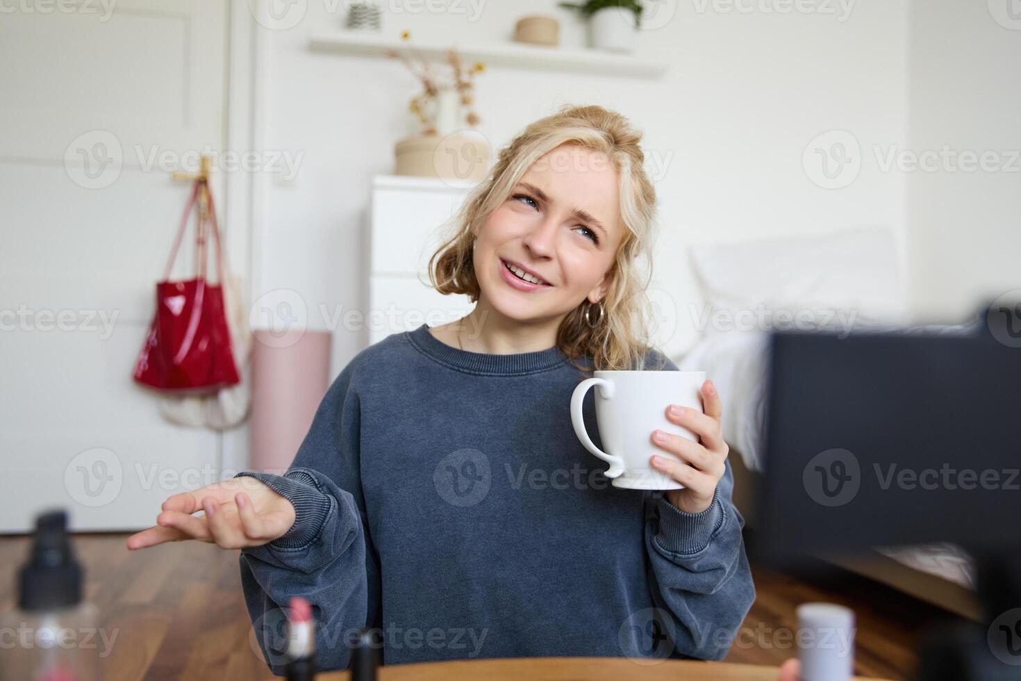 retrato do loiro jovem estilo de vida blogueiro, mulher registros do dela falando sobre vida e beleza, senta dentro frente do Câmera, detém xícara, bebidas chá, faz blog conteúdo para social meios de comunicação conta foto