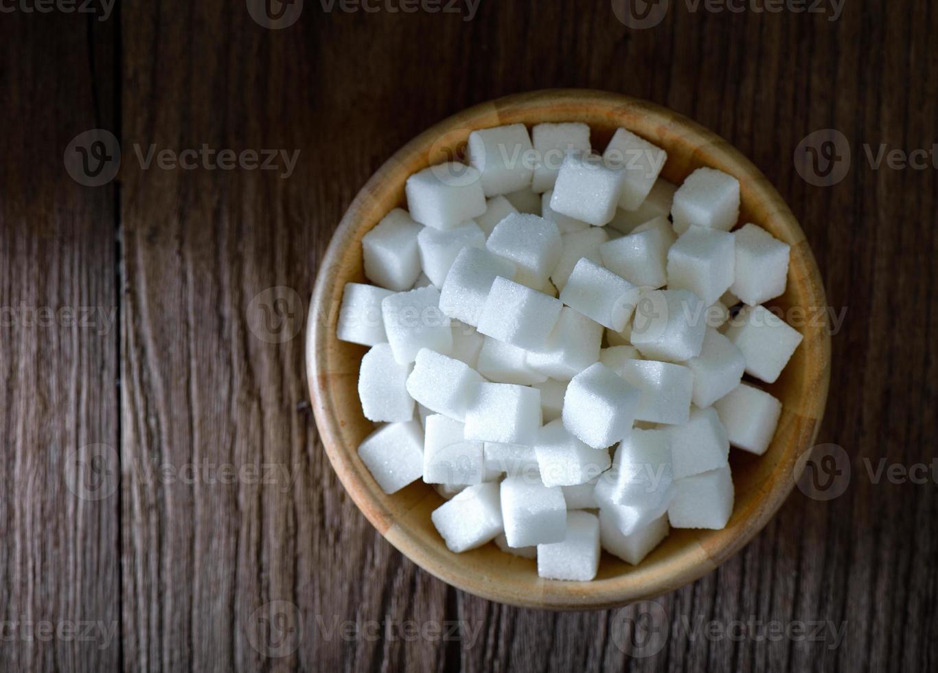 cubos de açúcar em uma tigela de madeira na mesa de madeira foto