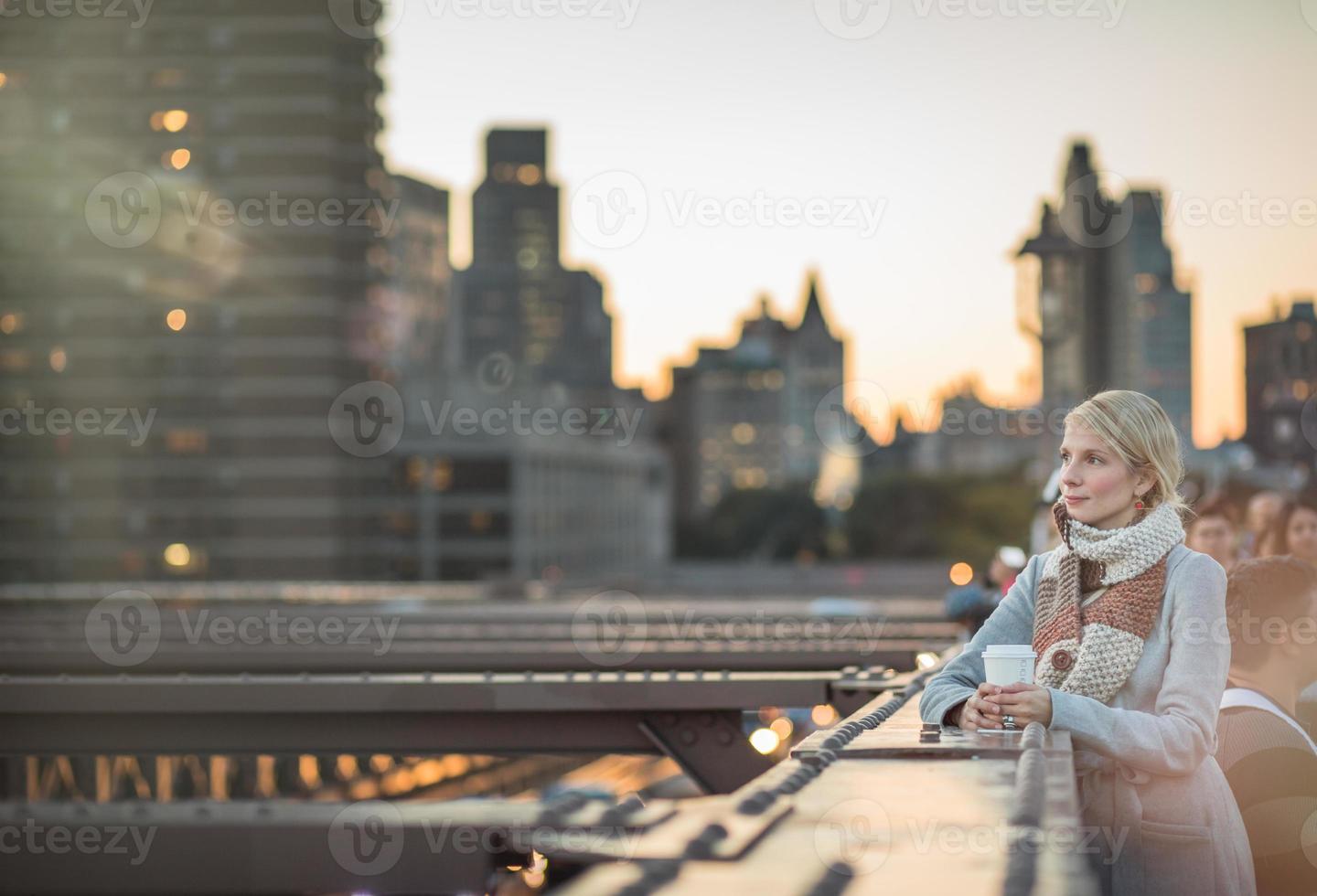 mulher na ponte do brooklyn olhando para manhattan com um café foto