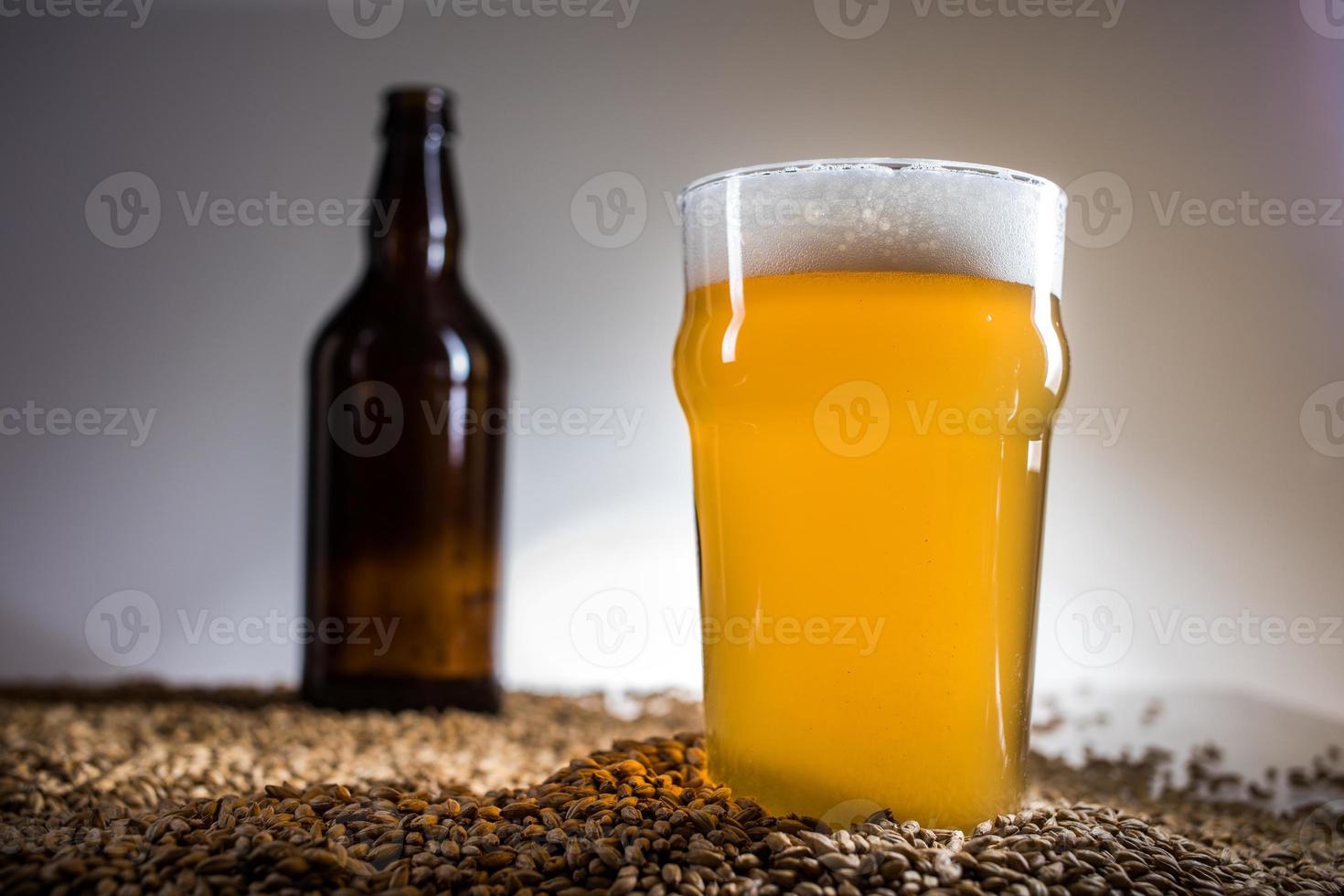 cerveja caseira loira e uma garrafa vazia de cerveja no grão de malte pislner foto