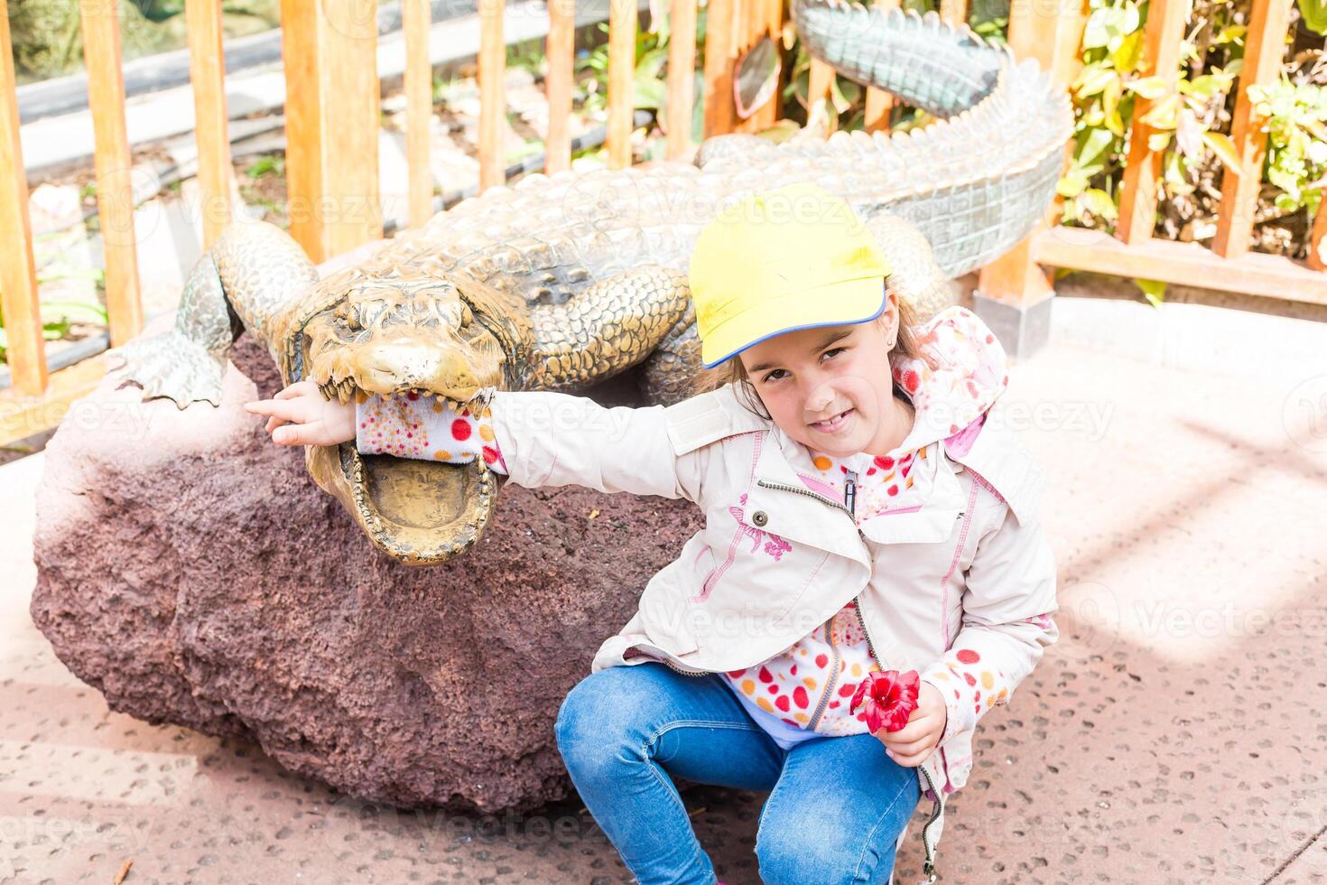 pequeno menina às a jardim zoológico com a monumento do uma crocodilo foto