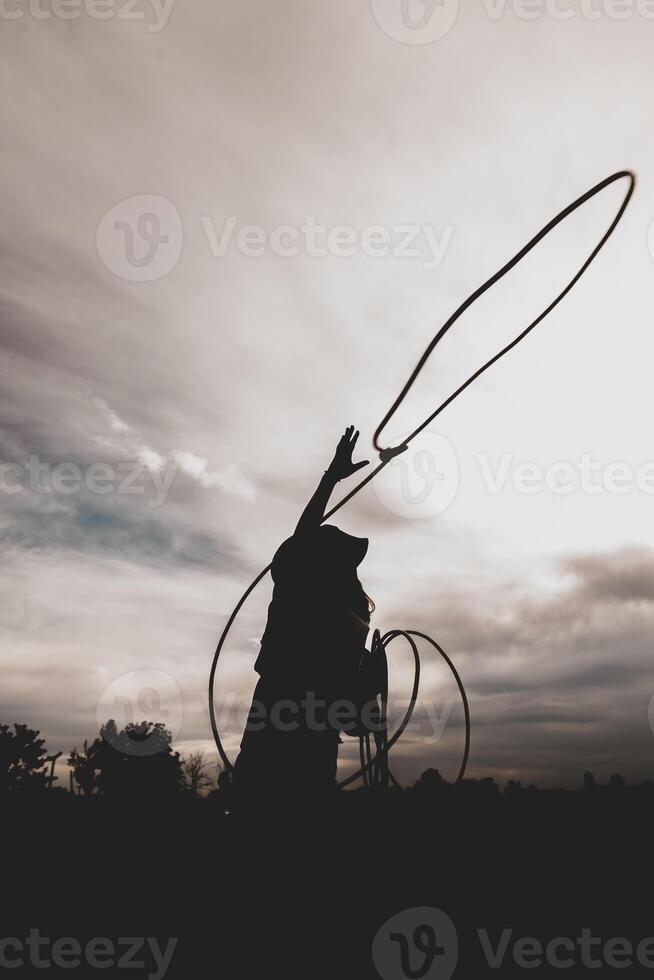 bonita chinês vaqueira jogando a laço dentro uma cavalo Pomar, pasto foto