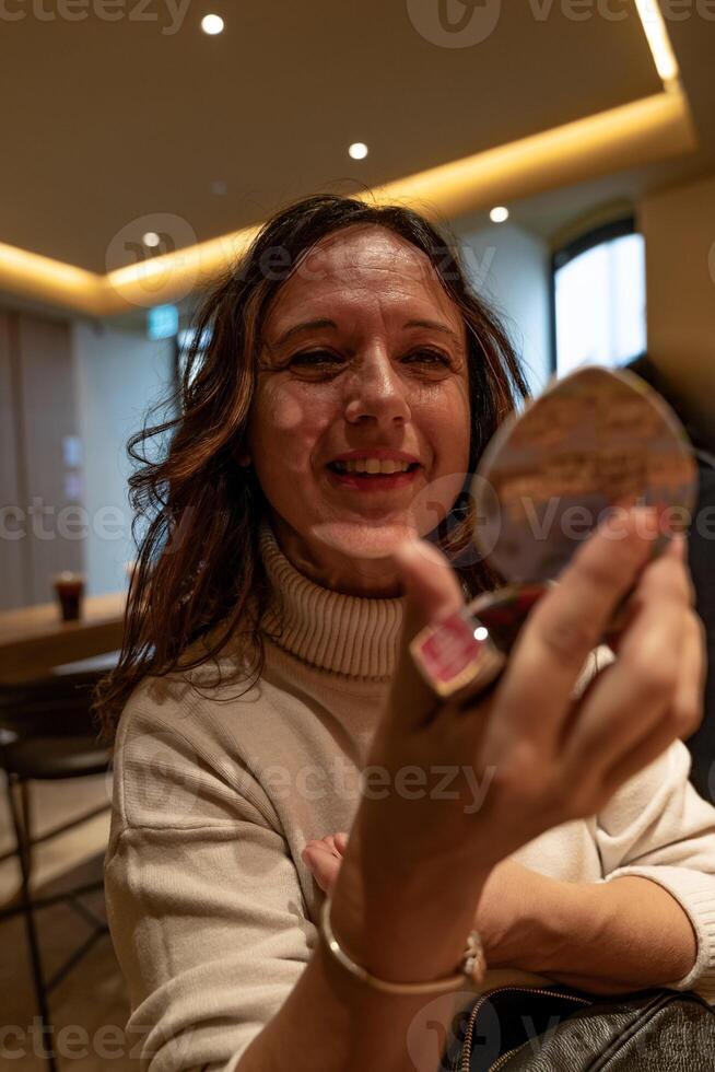 lindo maduro turista mulher colocando batom sentado dentro uma cafeteria em uma pausa foto