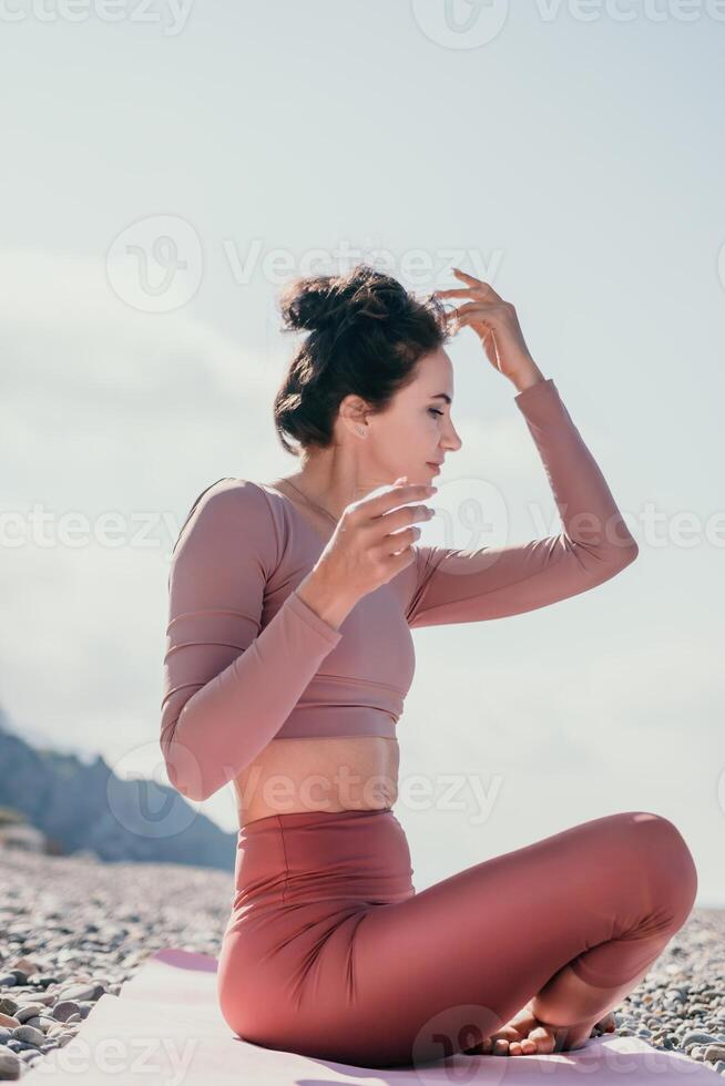 meio envelhecido bem olhando mulher com Preto cabelo, ginástica instrutor dentro perneiras e tops fazendo alongamento e pilates em ioga esteira perto a mar. fêmea ginástica ioga rotina conceito. saudável estilo de vida foto