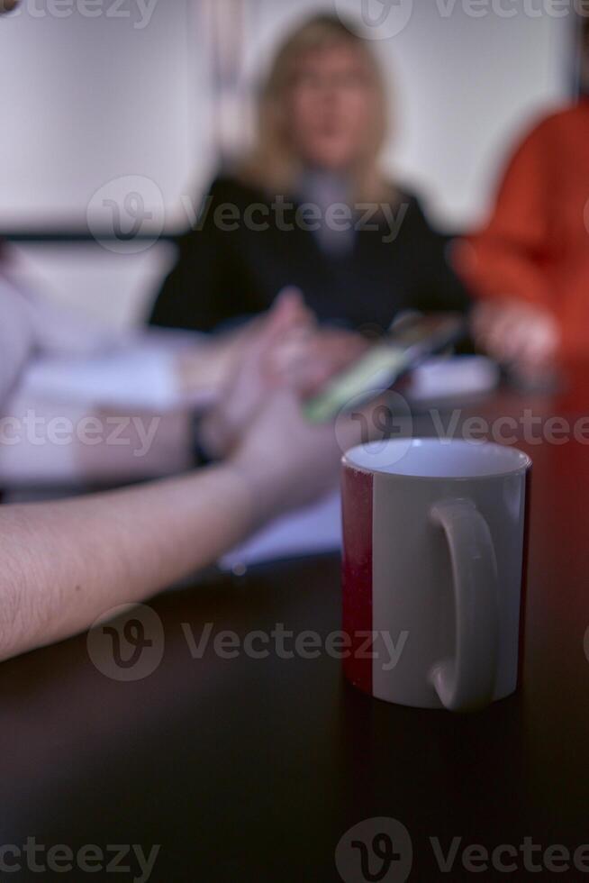 uma copo do café dentro a primeiro plano durante uma encontro dentro a escritório foto